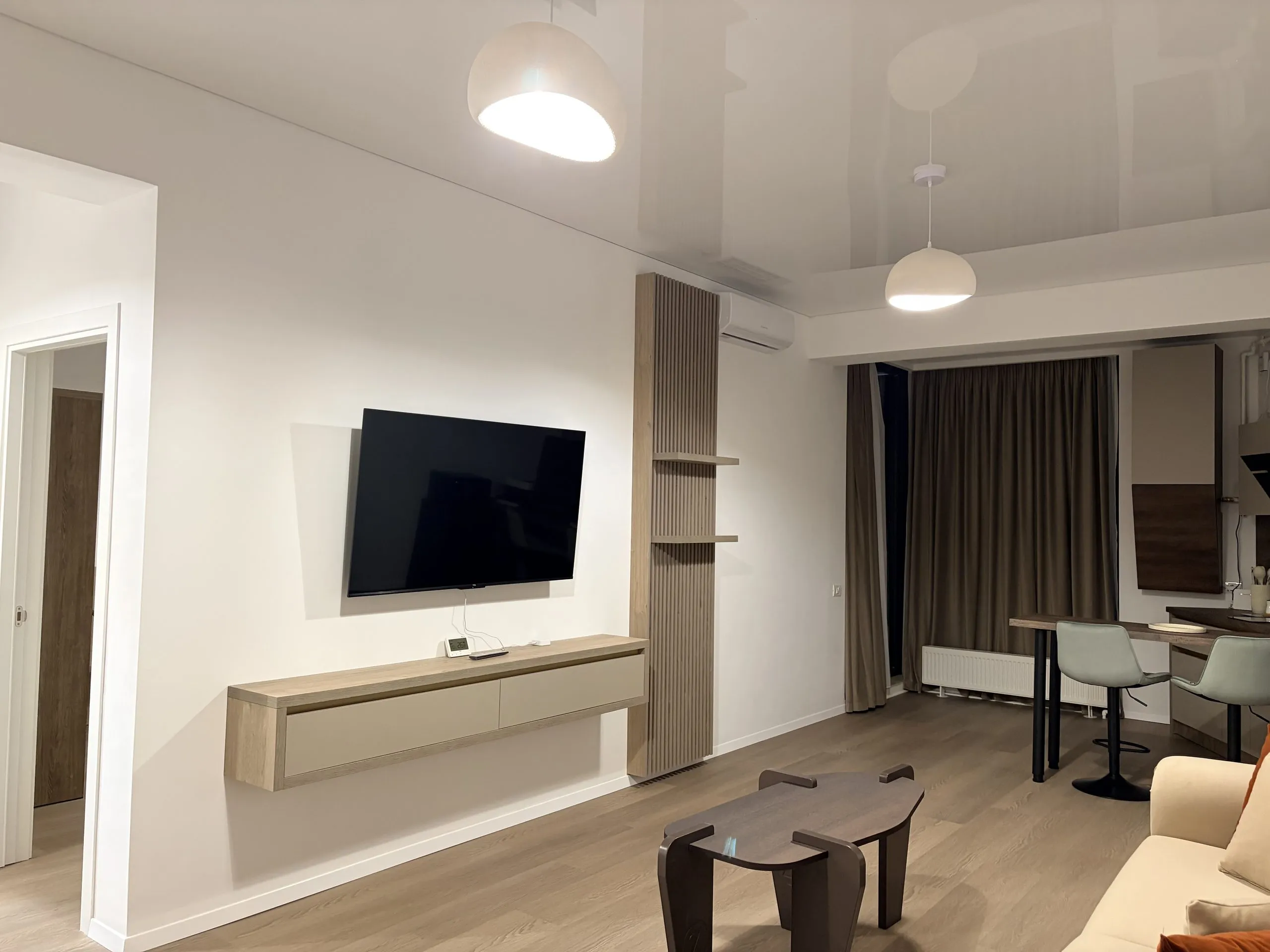 Living area with the television set into a wood-slat divider, the dining table and kitchen visible beyond