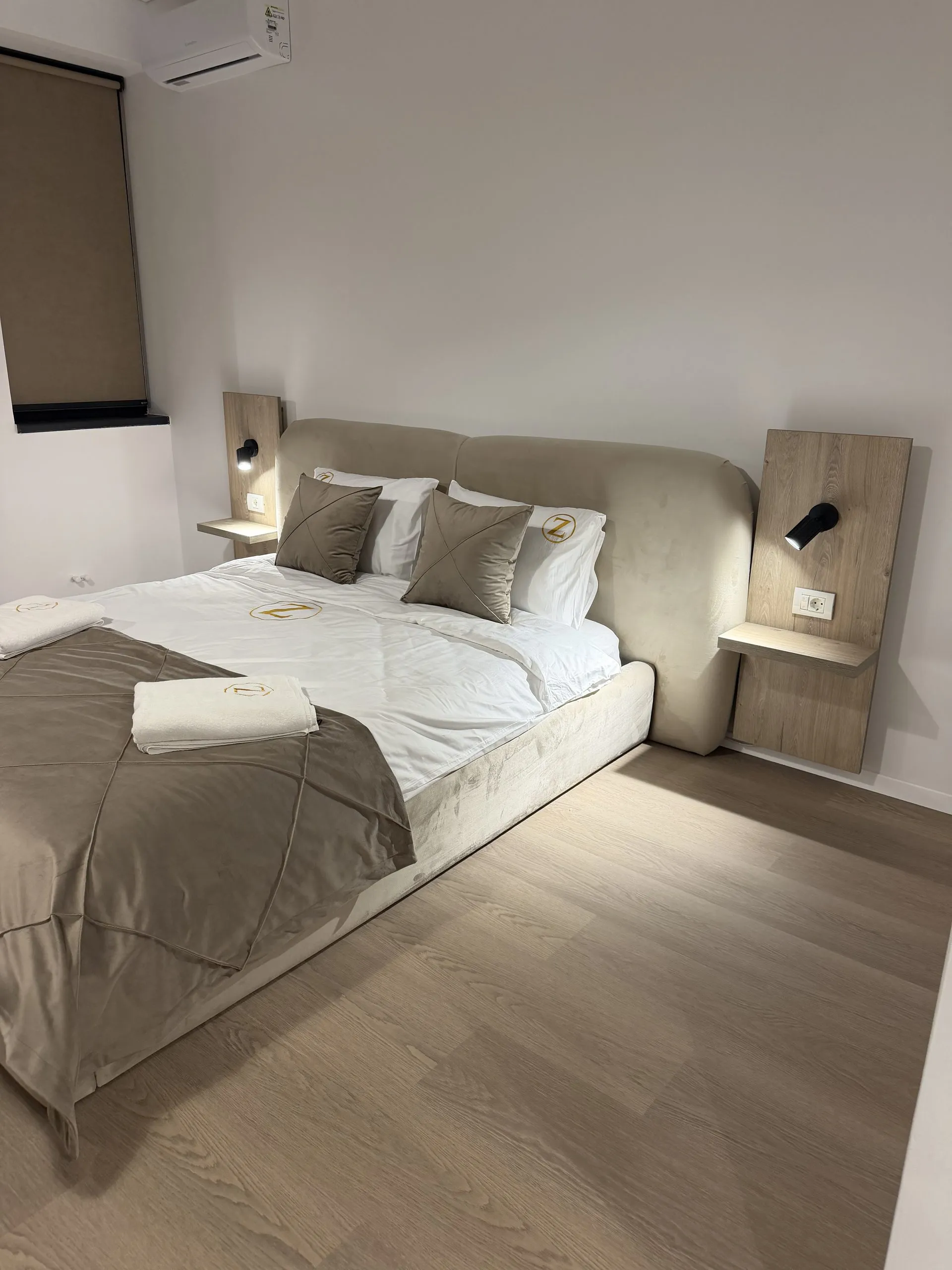 Studio bed with a taupe cover, an upholstered headboard set between wood side panels with integrated reading lights