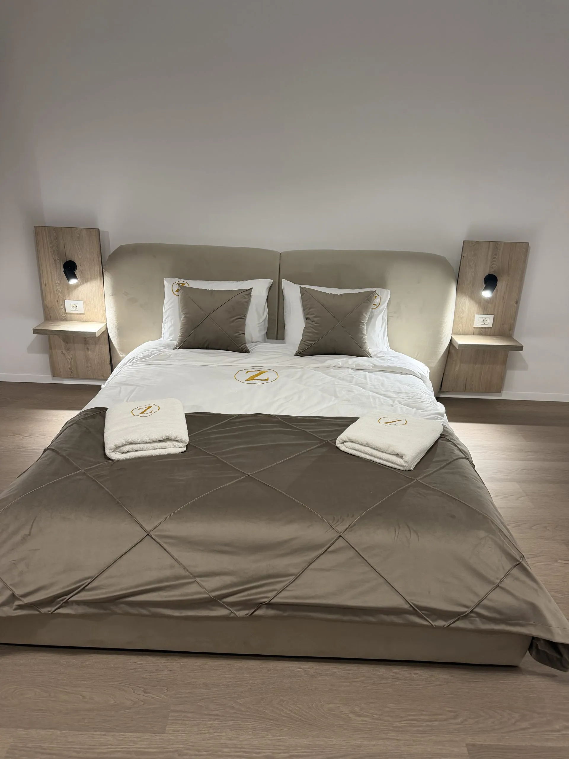 Studio bed seen straight on, made up with folded towels and monogrammed cushions